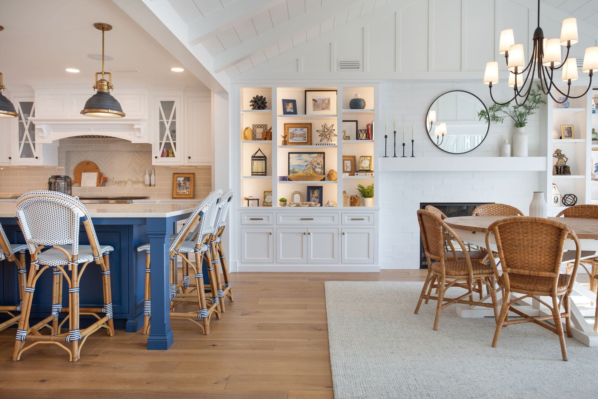 A kitchen with a blue island, wicker chairs, a table, and a fireplace.