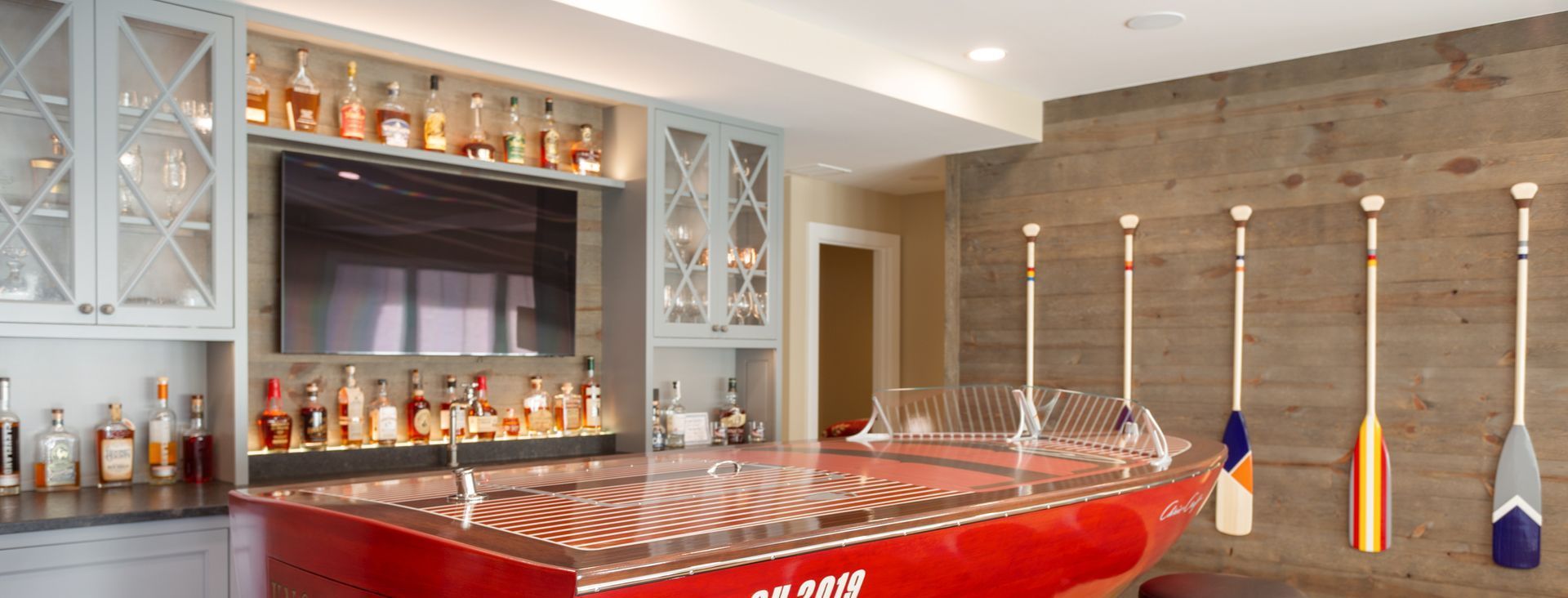 A home bar with a red boat shaped counter top and oars hanging on the wall.