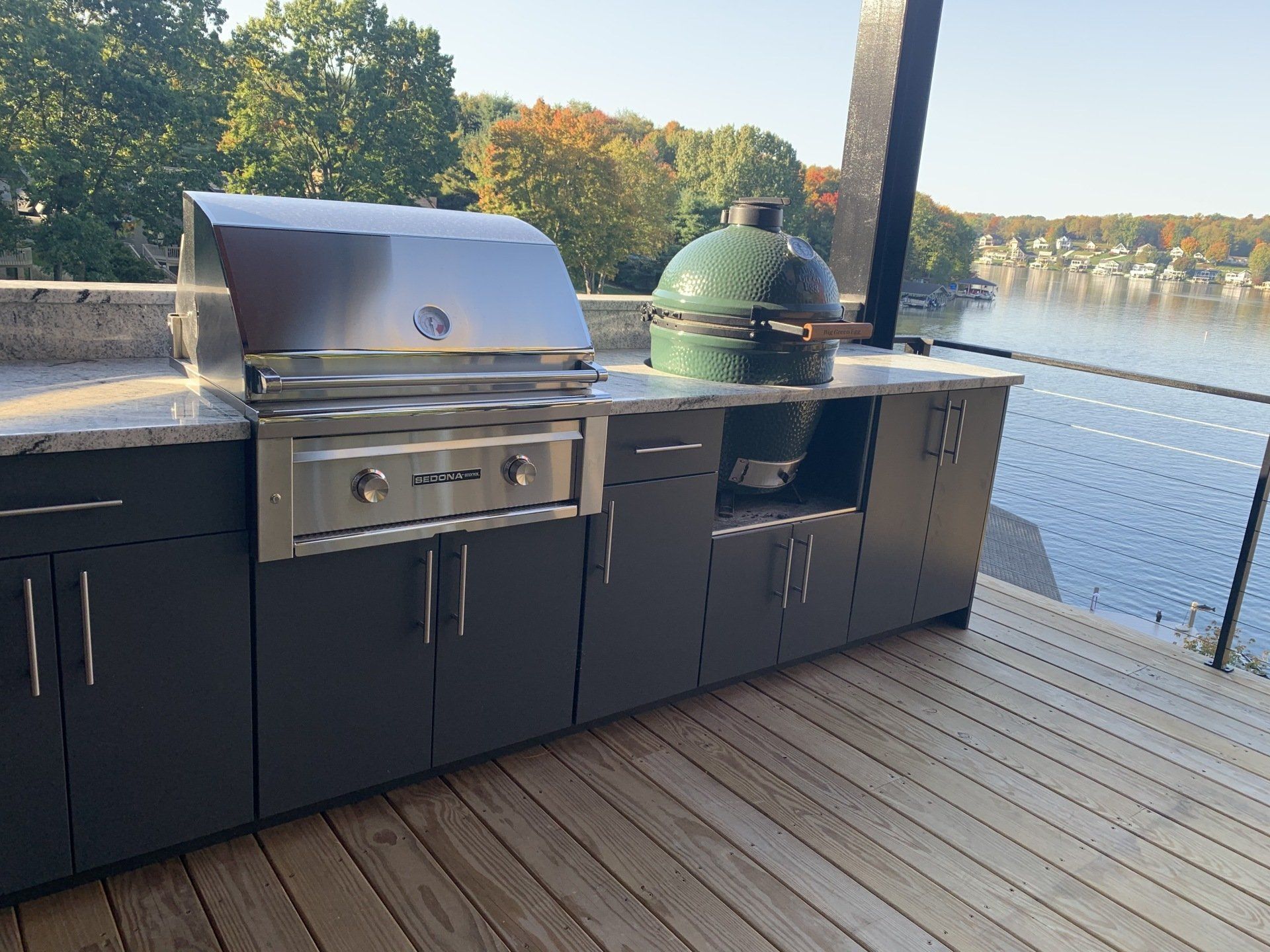 A large green grill is sitting on top of a wooden deck overlooking water. 
