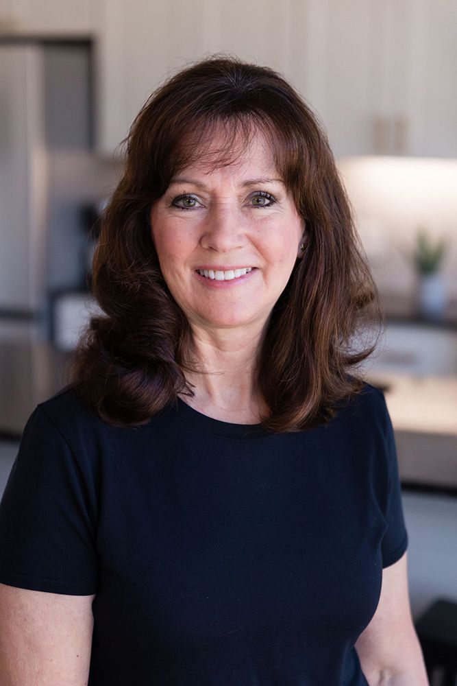 A woman in a black shirt is smiling in a kitchen.