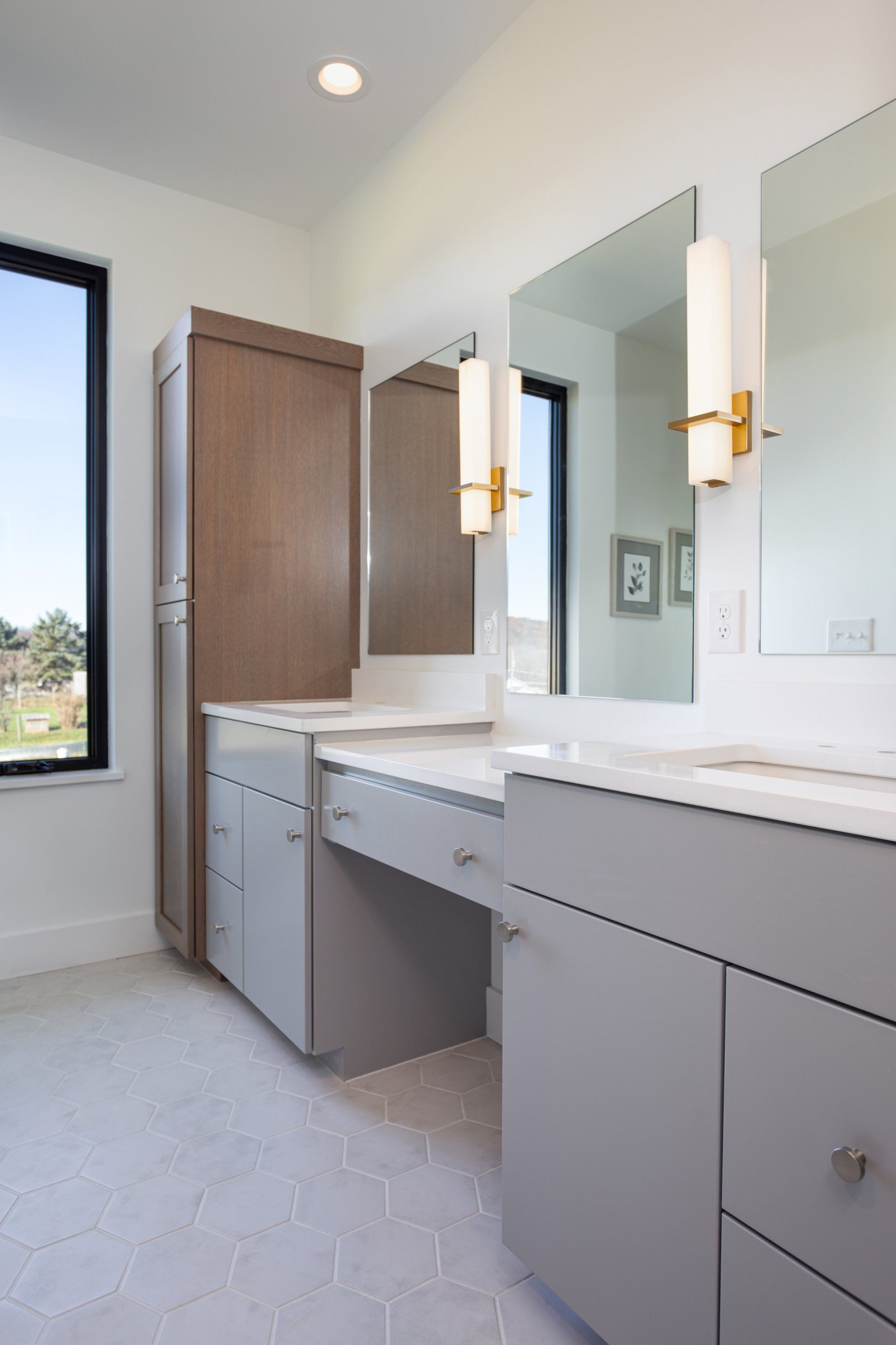 A bathroom with two sinks , two mirrors and a window.