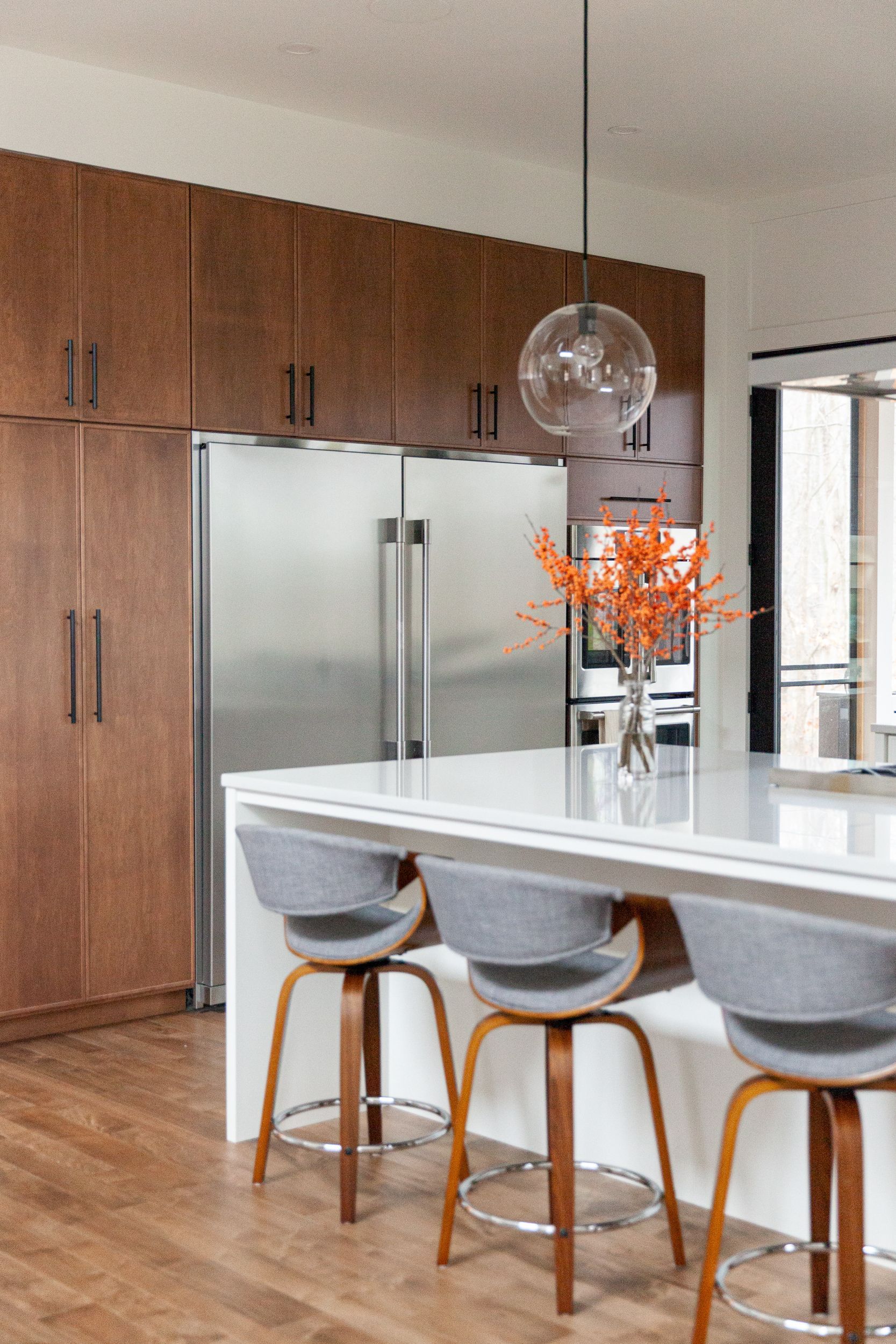 A kitchen with a large island, stools, a refrigerator, and a vase of flowers.