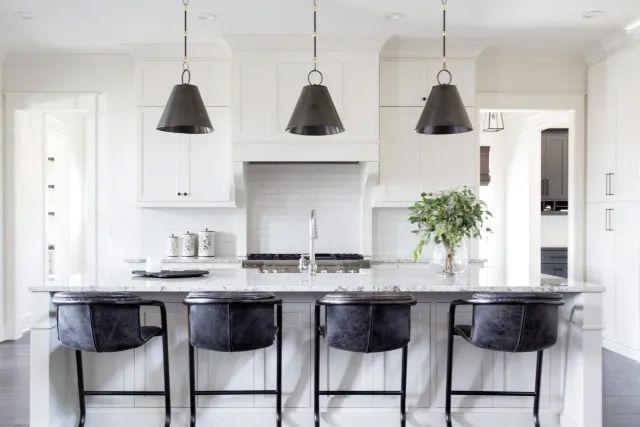 A kitchen with white cabinets and black bar stools.