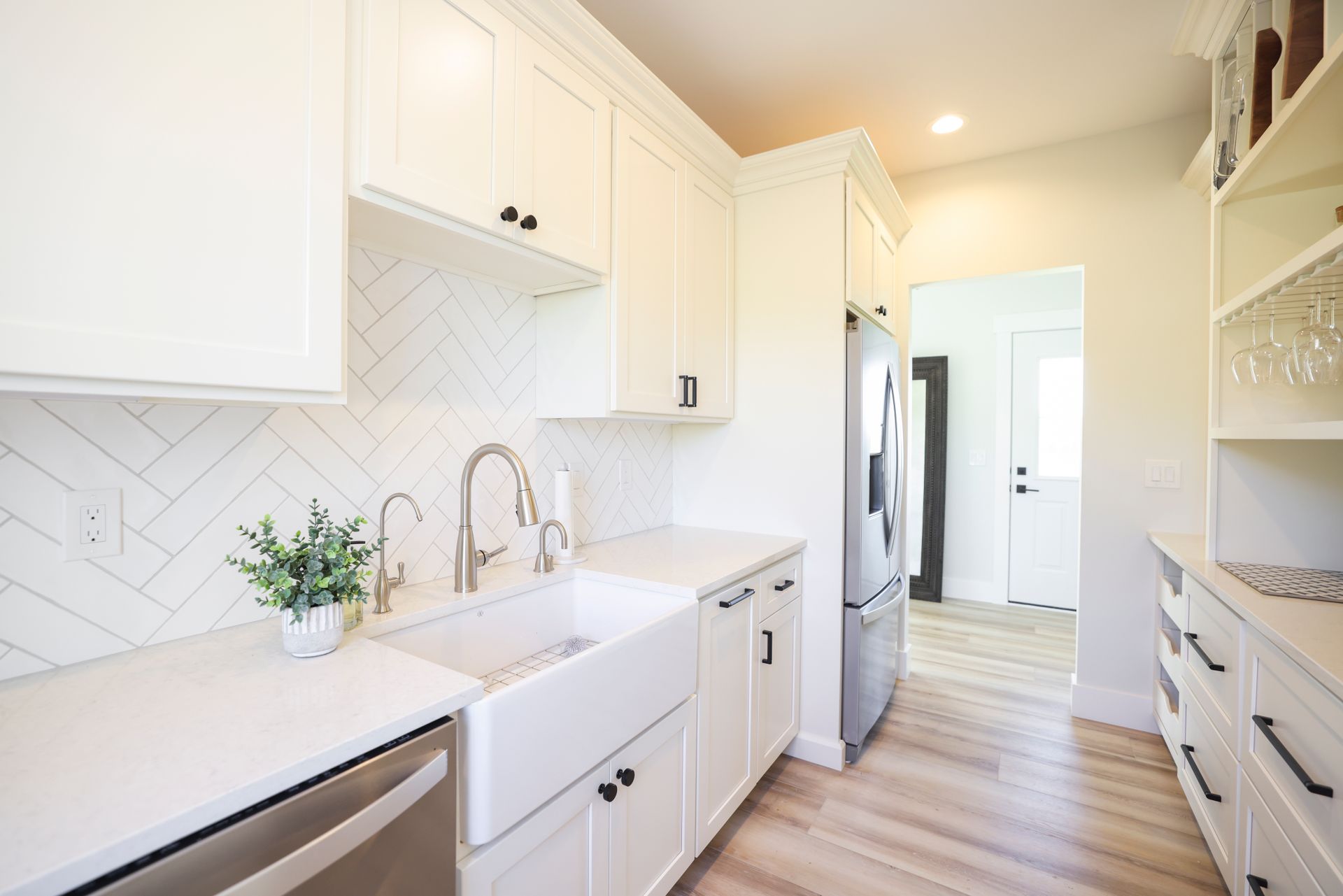 A kitchen with white cabinets , stainless steel appliances , a sink and a refrigerator.