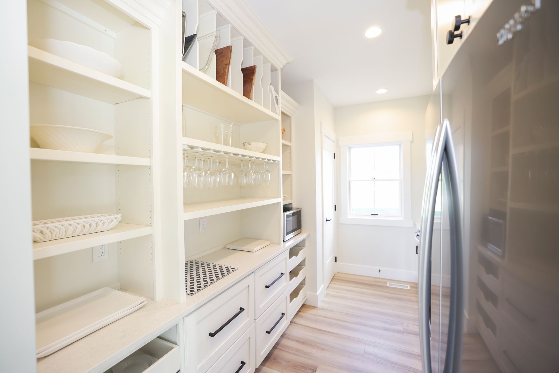 A kitchen pantry with white cabinets , drawers , a refrigerator and a window.