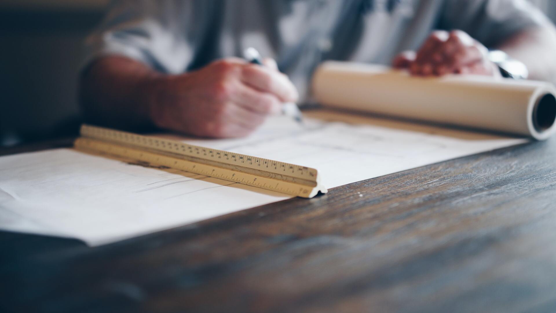 A person is writing in a notebook on a wooden table.