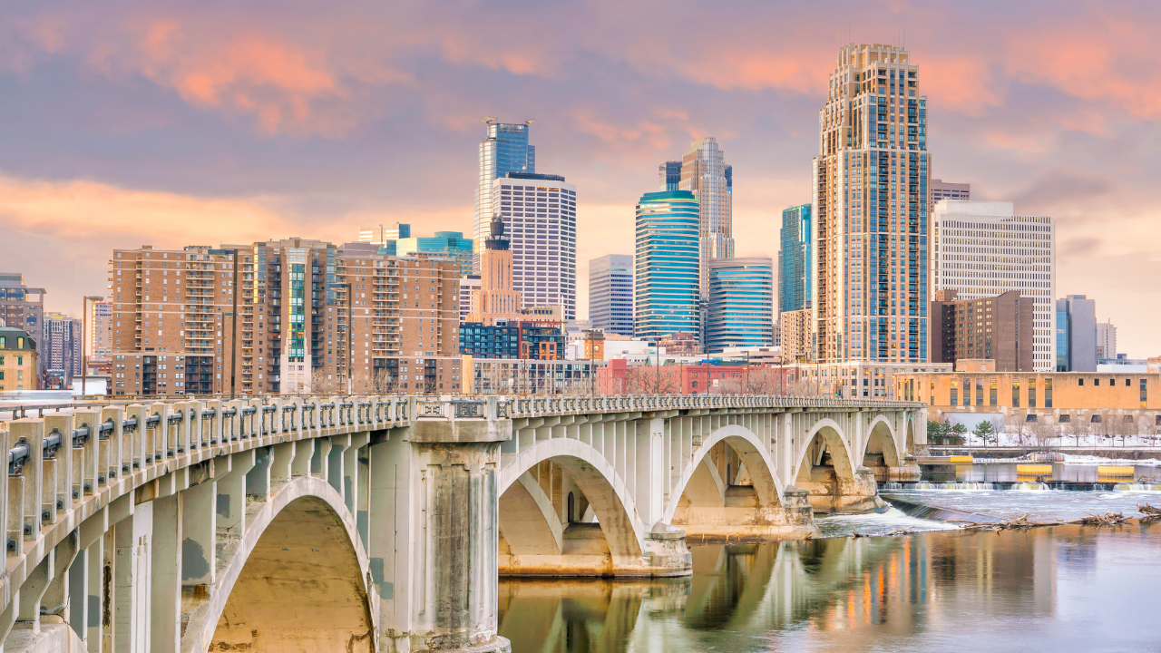 Aerial view of Minneapolis, Minnesota, skyline at sunset over the Mississippi River with bridges, trees, and buildings.