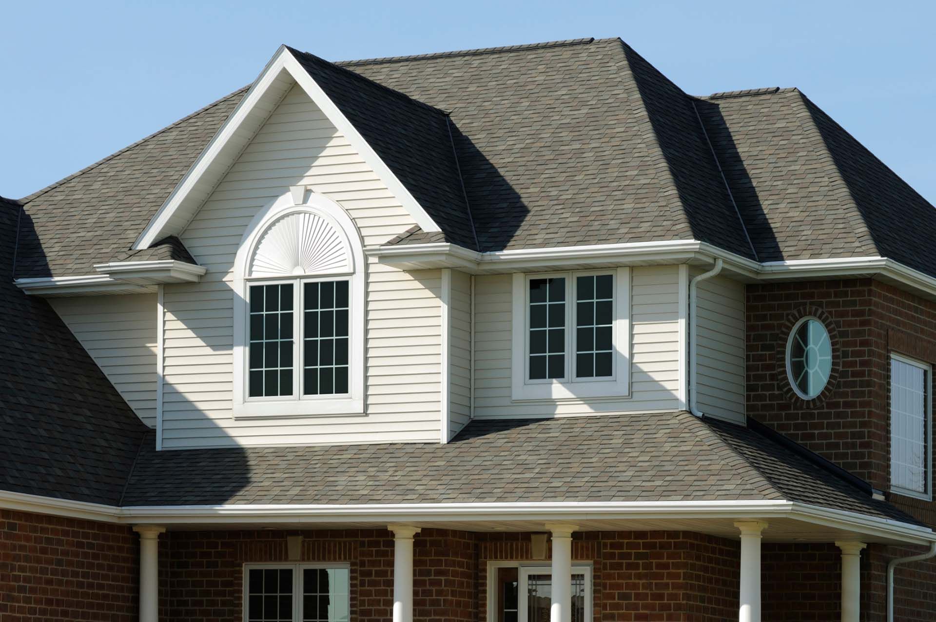 View of a white house with gray new asphalt shingle roof against the blue sky