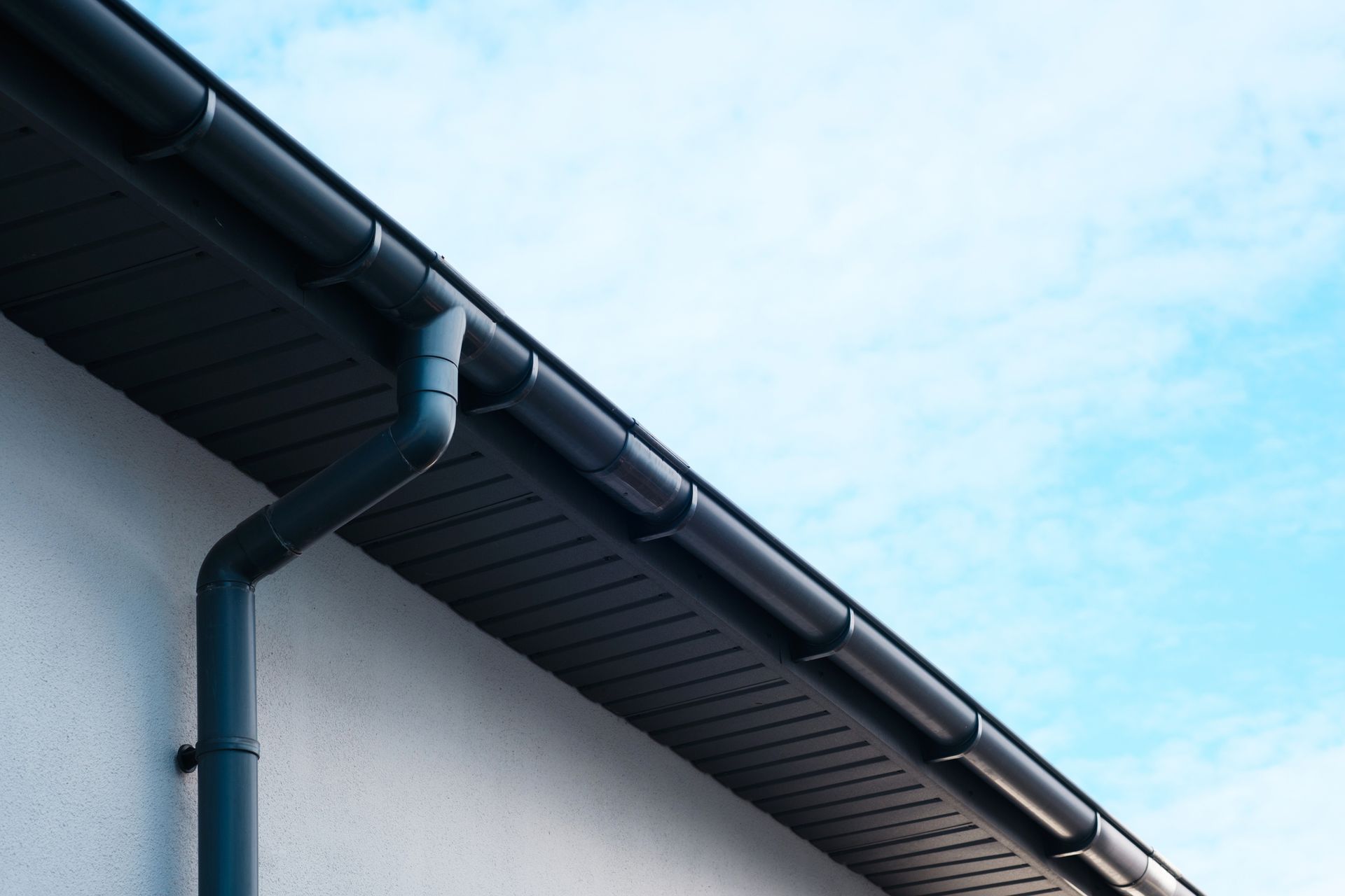 Modern building gutter system installed by gutter repair contractor under clear blue sky outdoors.