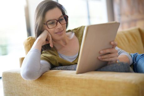 A woman is sitting on a couch using a tablet computer.