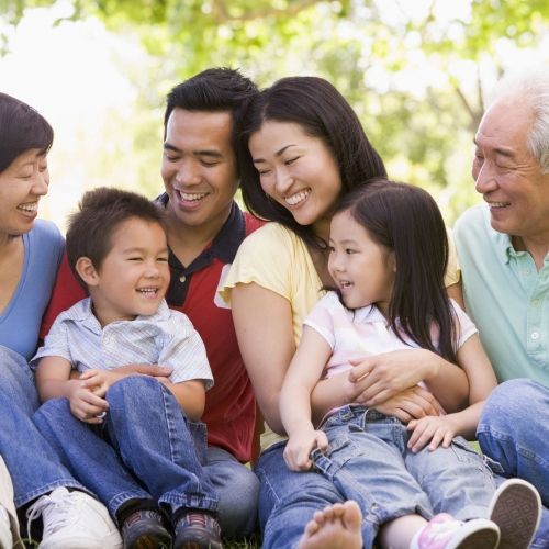 A family is sitting on the grass together and smiling.