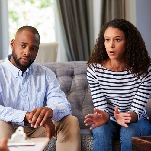 A man and a woman are sitting on a couch talking to each other.