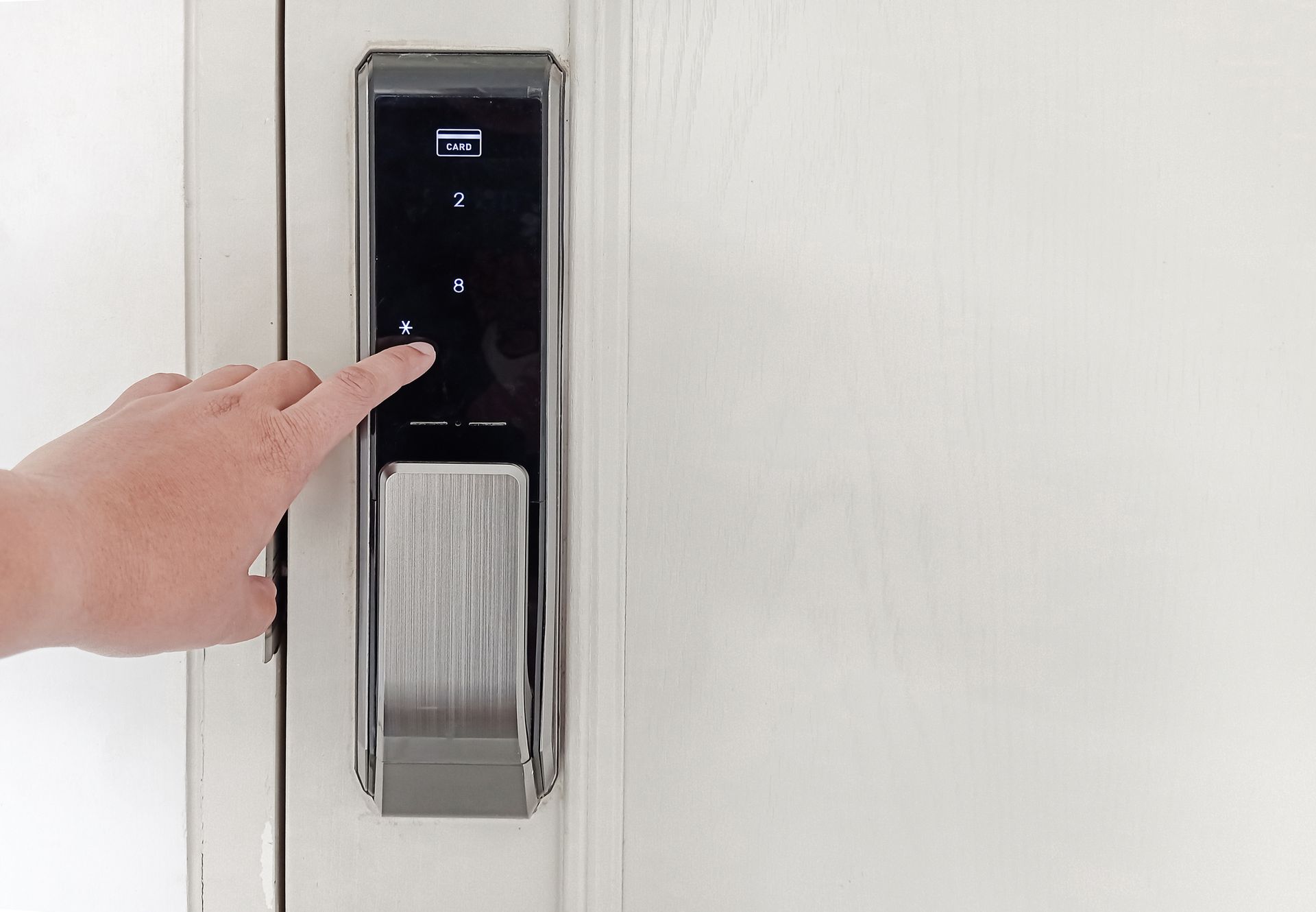 Hand pressing a number on a digital door lock with numbers displayed on the screen. White door.