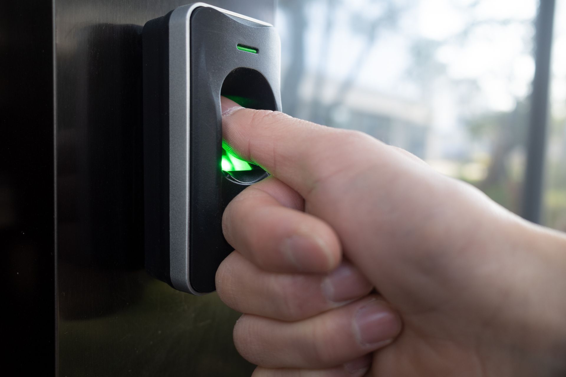 Person's finger pressing a lit-up keypad on a brick wall. An adjacent panel of call buttons is visible to the left.