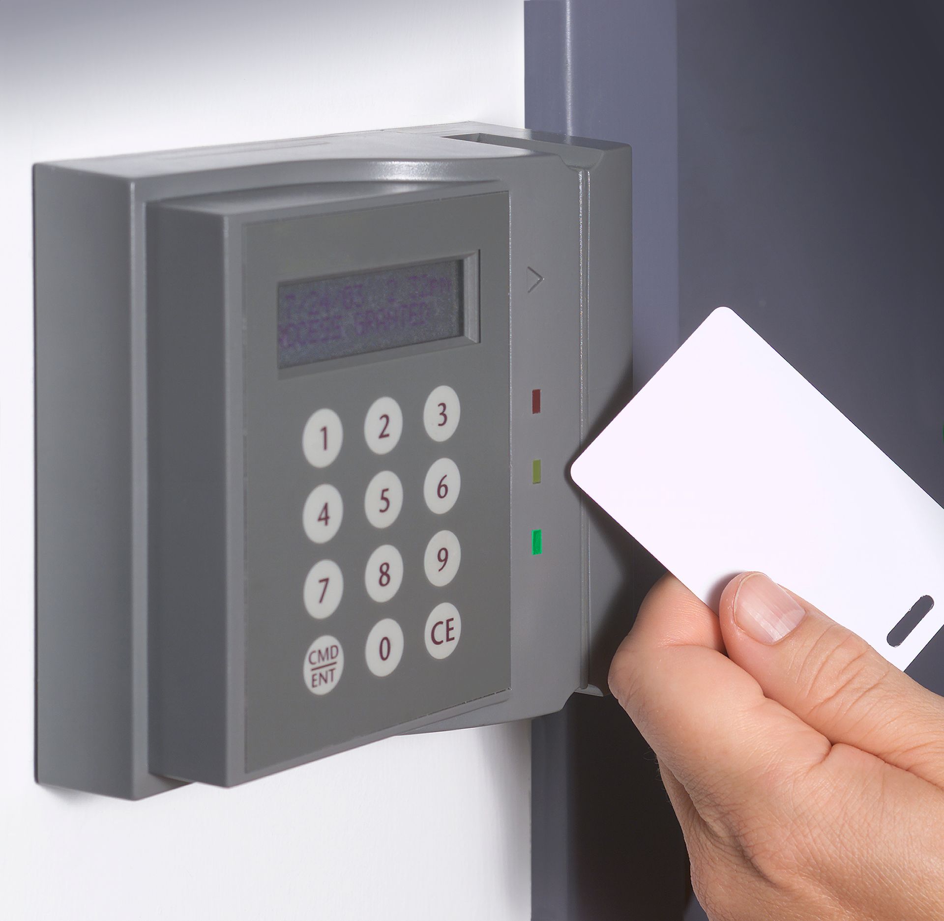 Person's finger pressing a lit-up keypad on a brick wall. An adjacent panel of call buttons is visible to the left.