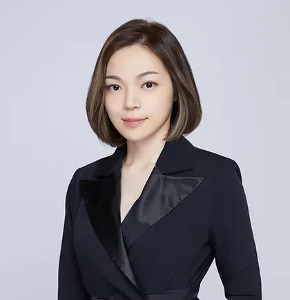 A woman in a black suit is standing in front of a white background.
