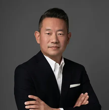 A man in a suit and tie is standing with his arms crossed.