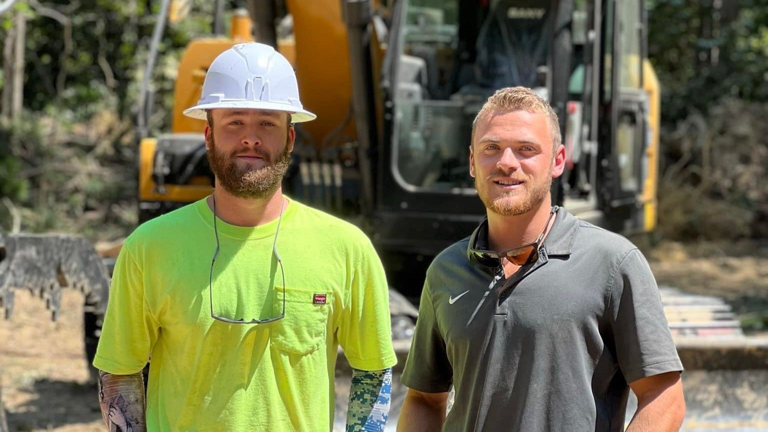 Two construction workers are standing next to each other in front of a bulldozer.