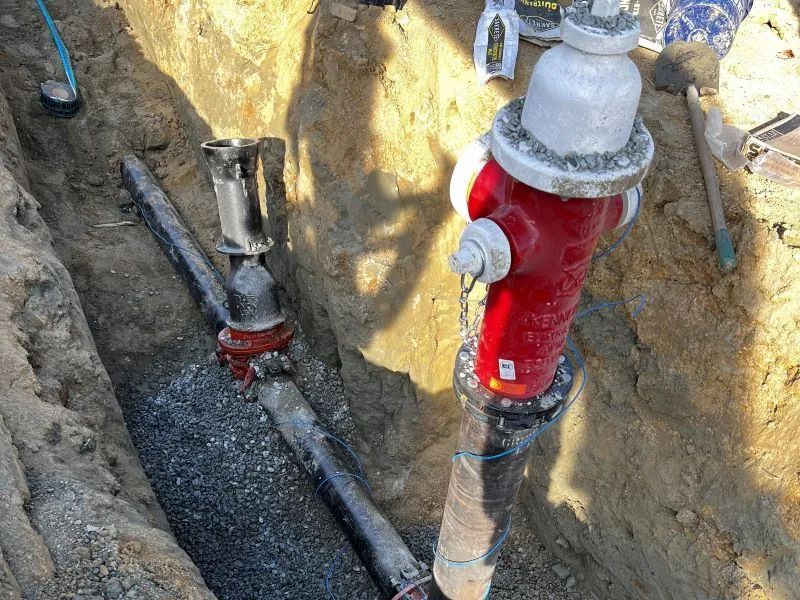 A red fire hydrant is sitting in the dirt next to a pipe.