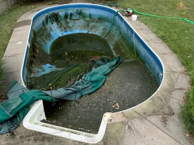A dirty swimming pool with a green tarp on the side of it.