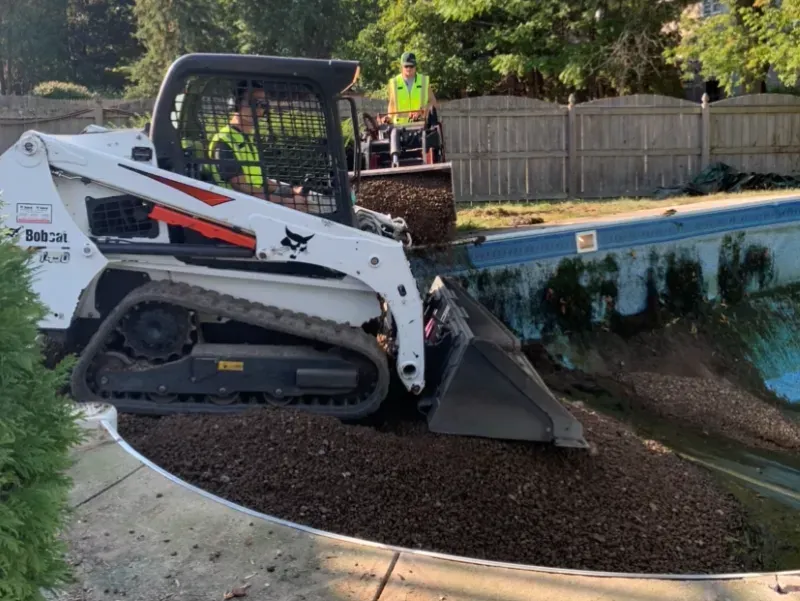 A bobcat is moving dirt around a swimming pool.