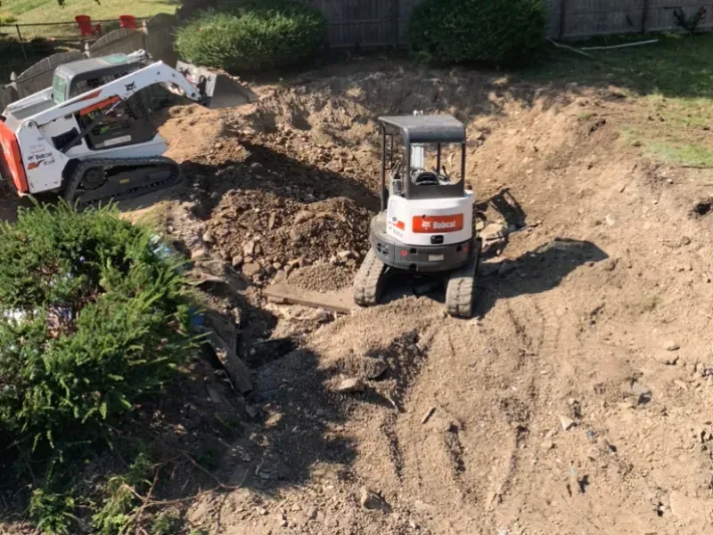 A bulldozer is digging a hole in the dirt in a backyard.
