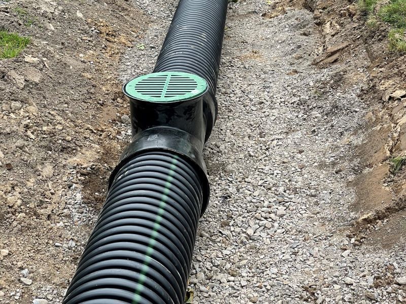 A black pipe with a green lid is sitting in the dirt.