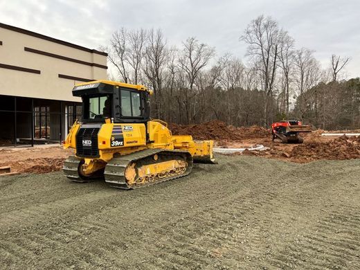 A yellow bulldozer is sitting in a dirt field in front of a building.