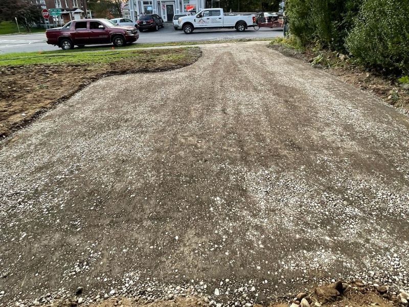 A red car is parked in a gravel lot next to a white truck.