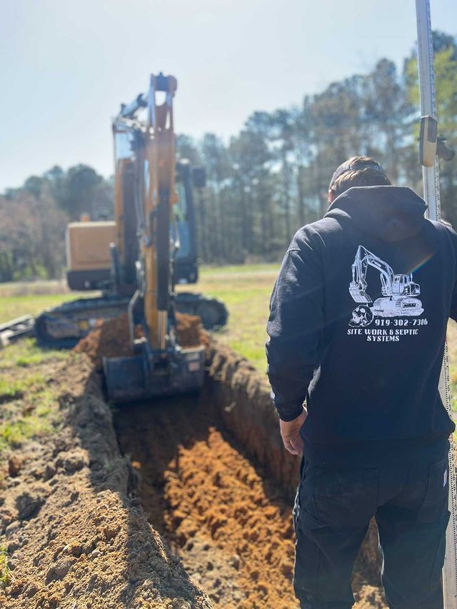 A man is standing in front of an excavator in a field.