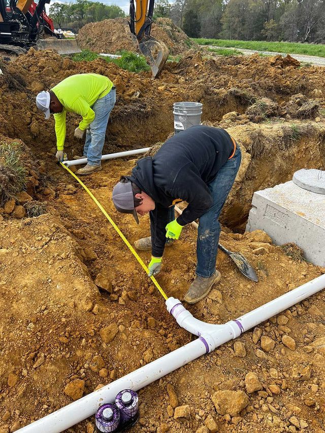 Two men are measuring pipes in the dirt.
