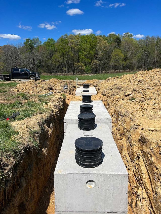 A row of concrete septic tanks are being installed in a trench.