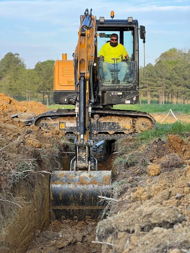 A man is driving an excavator in a dirt field.