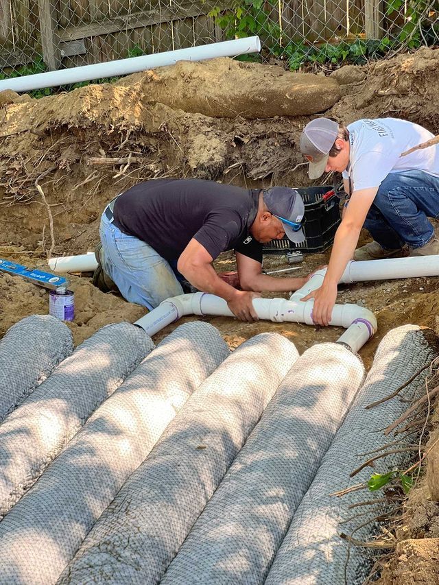 Two men are working on a drainage system in the dirt.