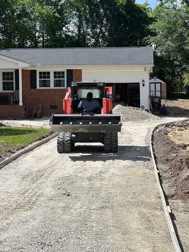 A bulldozer is driving down a gravel driveway in front of a house.