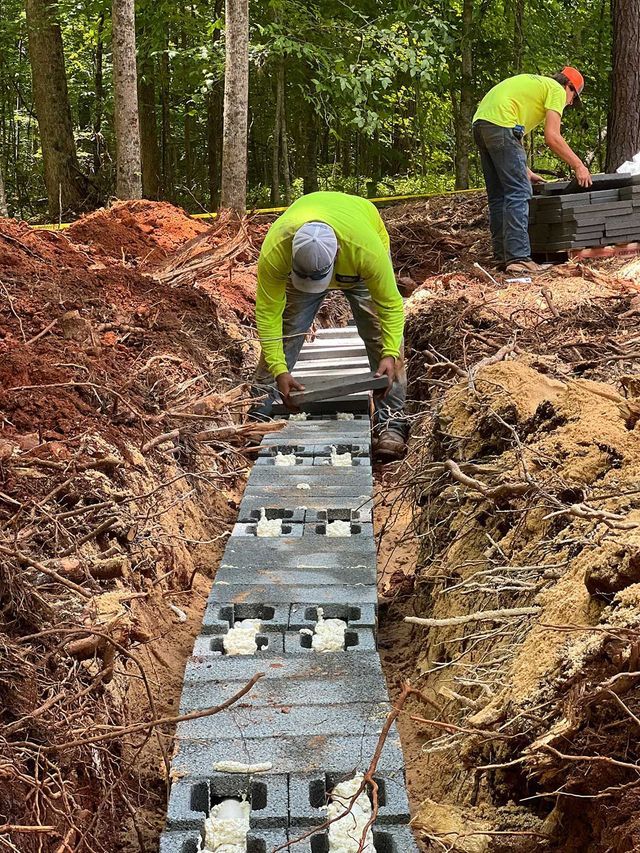 Two men are working on a drainage system in the woods.