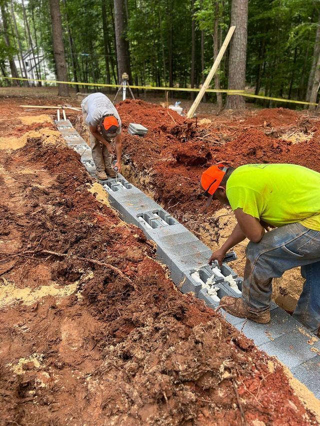 Two construction workers are working on a concrete wall in the dirt.