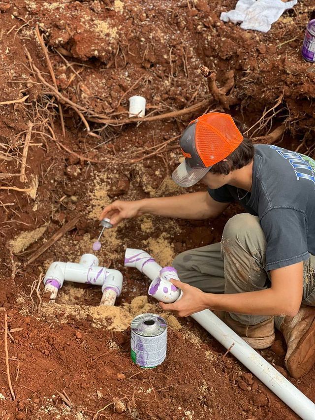 A man is working on a pipe in the dirt.
