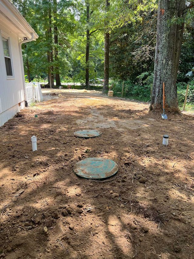 There is a septic tank in the middle of the dirt in front of a house.
