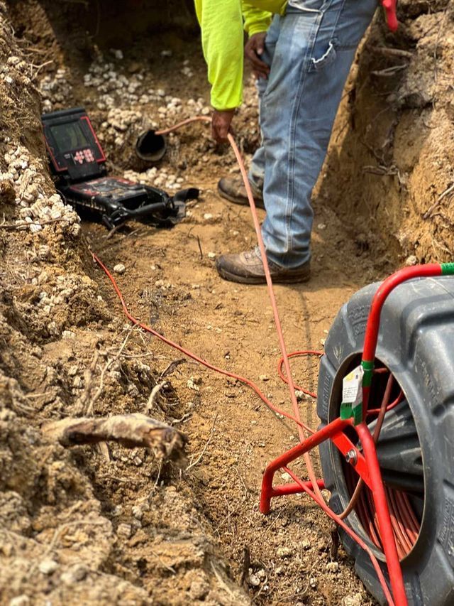 A man is standing in the dirt next to a tire and a camera.