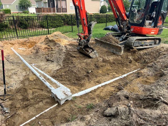 A red excavator is digging a hole in the dirt in front of a house.