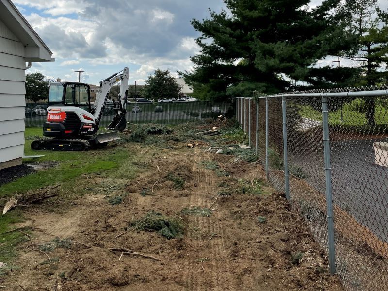 A small excavator is sitting in the dirt next to a chain link fence.