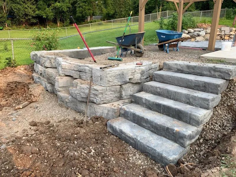 A stone wall and stairs are being built in a backyard.