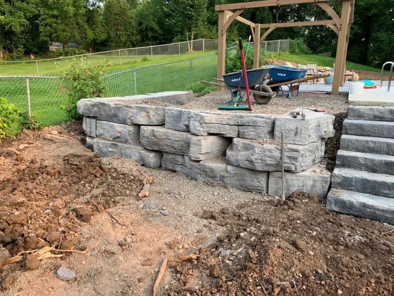 A stone wall and stairs are being built in a backyard.