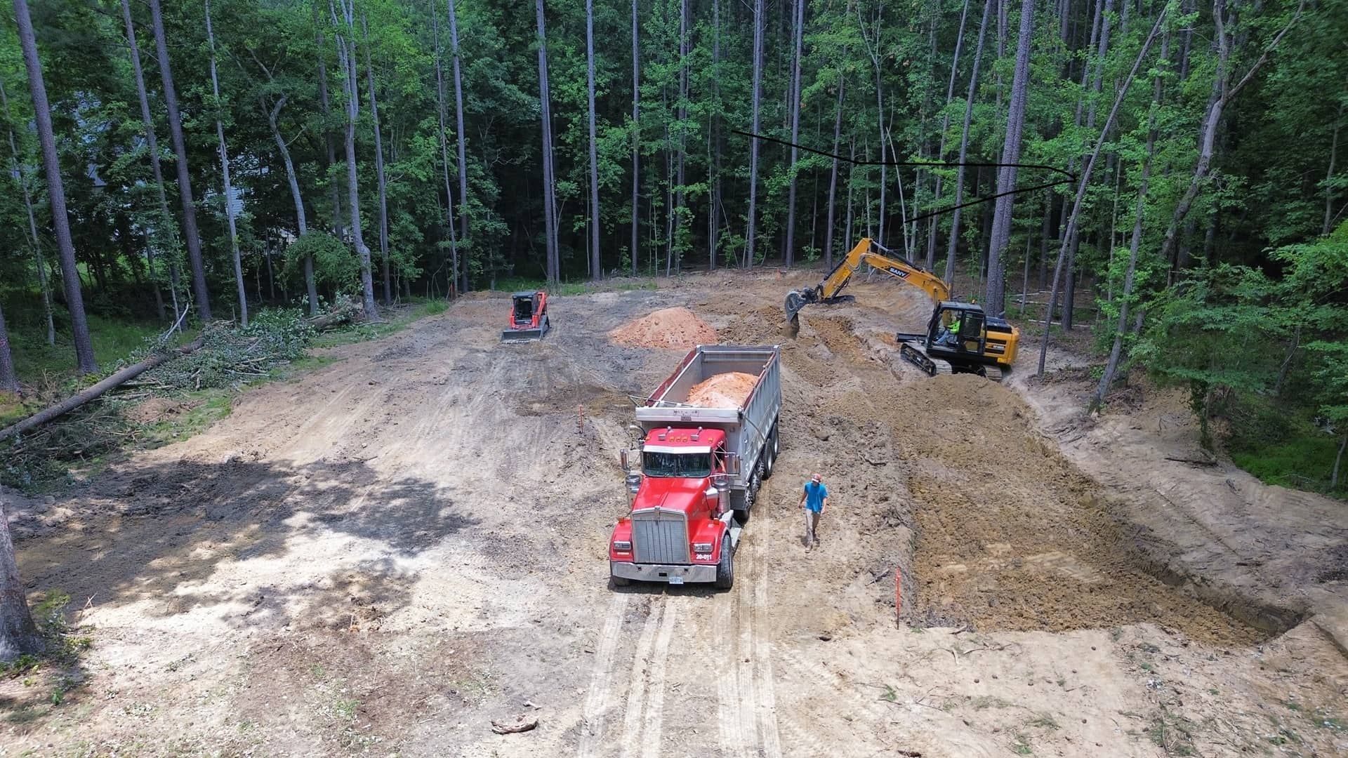 An aerial view of a dump truck driving down a dirt road in the woods.