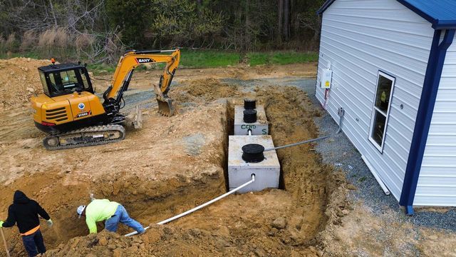 A man is digging a hole in the dirt next to a house.