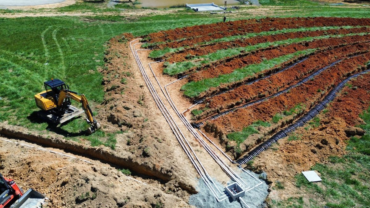 A yellow excavator is digging a trench in a field.