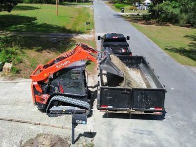 A bulldozer is loading dirt into a dumpster next to a truck.