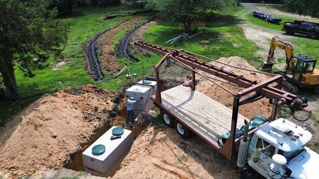 An aerial view of a truck loading a septic tank into a hole.