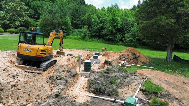 A yellow excavator is digging a hole in the dirt in a yard.